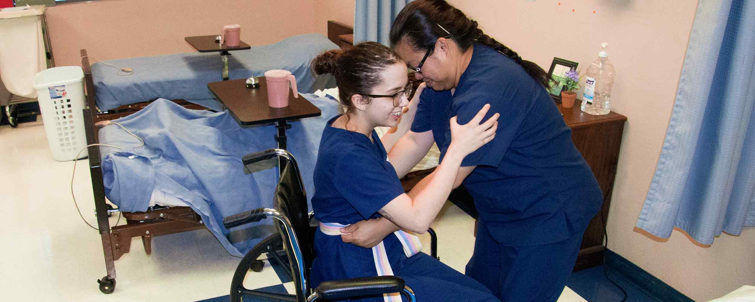 photo of nursing assistant student helping a fellow student who is in a wheelchair