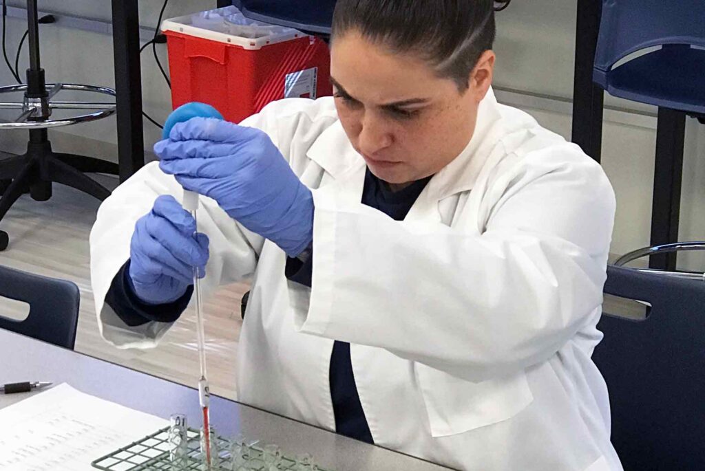 Medical laboratory technician student sitting at desk in lab filling test tubes.