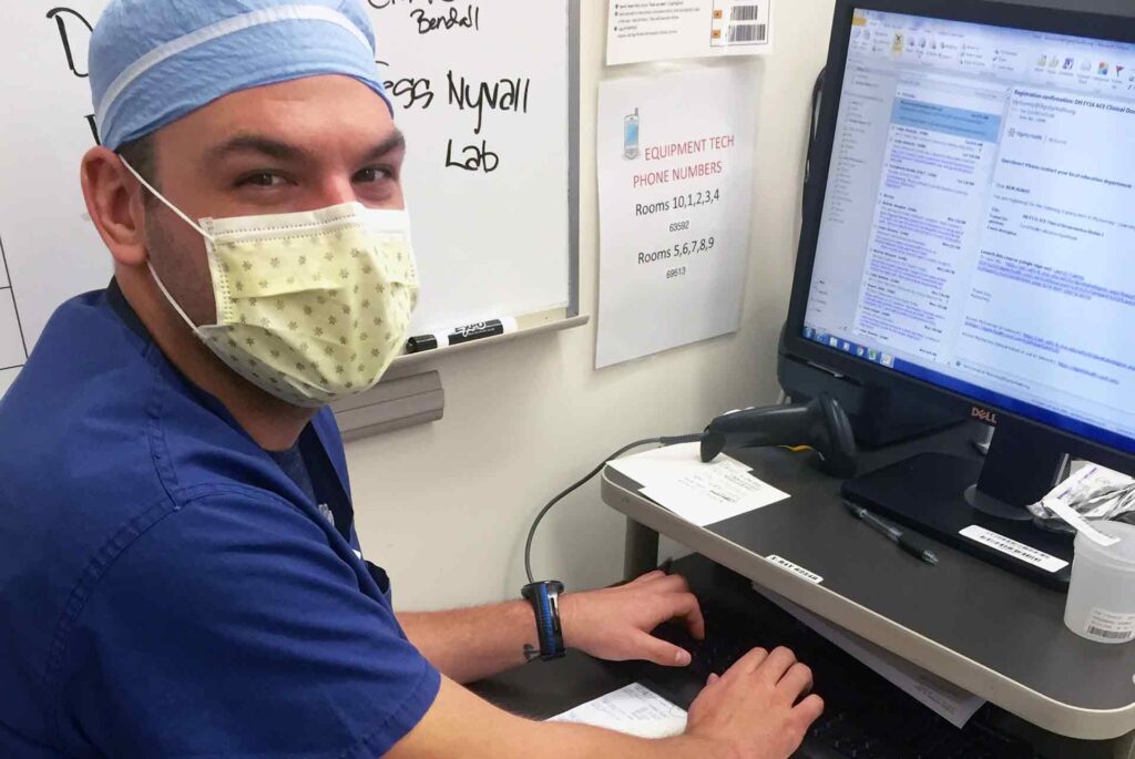 mid-range photo of nurse in PPE and mask sitting in front of computer