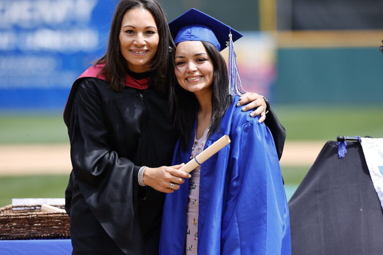 Colorado Springs campus director’s arm around student in cap and gown at graduation ceremony.