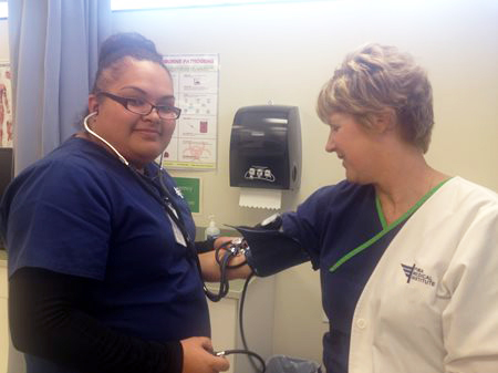 female student in scrubs checking blood pressure of a faculty member.