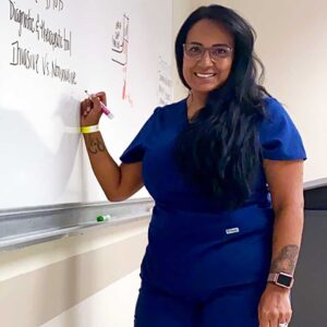 Woman in scrubs writing on white board while looking at camera