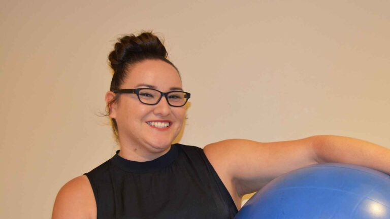female student smiles at camera while holding large balance ball