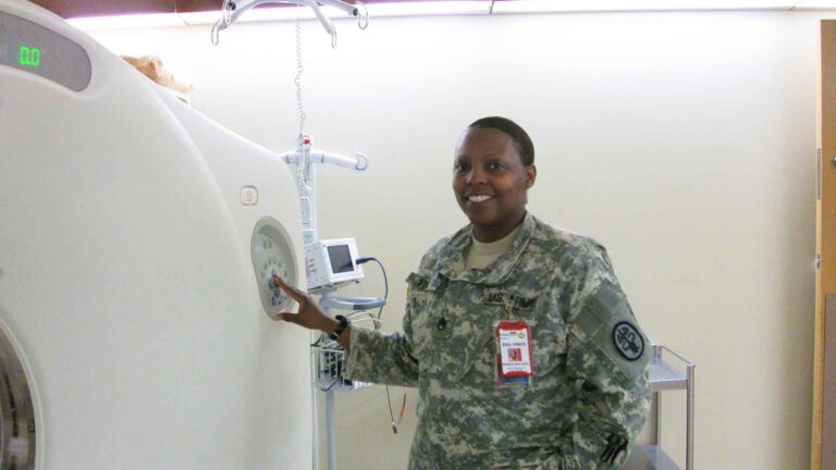 female solider in army uniform standing near large radiologic machine.