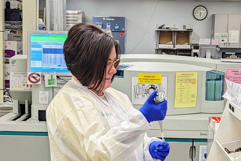 woman in PPE in medical lab, working with a test tube and liquids