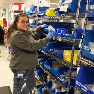 woman in jeans and sweatshirt standing in a storage room of medical equipment and supplies