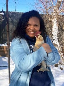 African-American woman standing outside while holding a live chicken and smiling at the camera