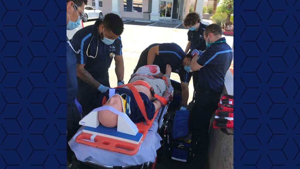 four Las Vegas paramedic students work on a simulation manikin on a stretcher outside the lab classroom