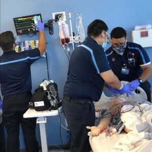 Paramedic students surround a hospital bed with a simulation manikin, practicing hands-on skills