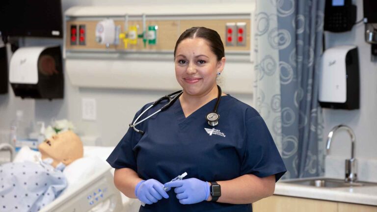 Female nursing student looking at the camera smiling, wearing Pima Medical scrubs.