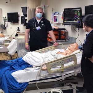 female and male students in scrubs posing in the nursing simulation lab near a table with a manikin patient