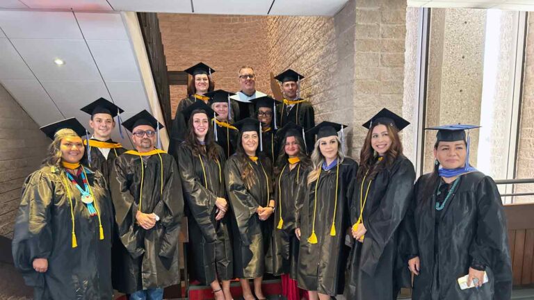 male and female students in blue caps and gowns pose for a picture prior to lining up to walk in to their graduation ceremony