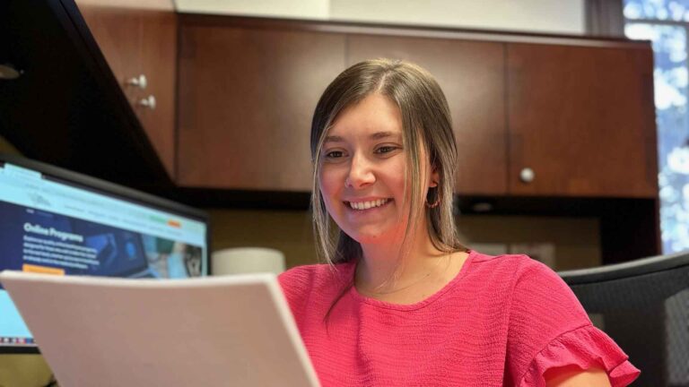 photo of Pima Medical’s online in health care administration associate and bachelor’s degree graduate, Taylor M. working at her desk in a medical office.