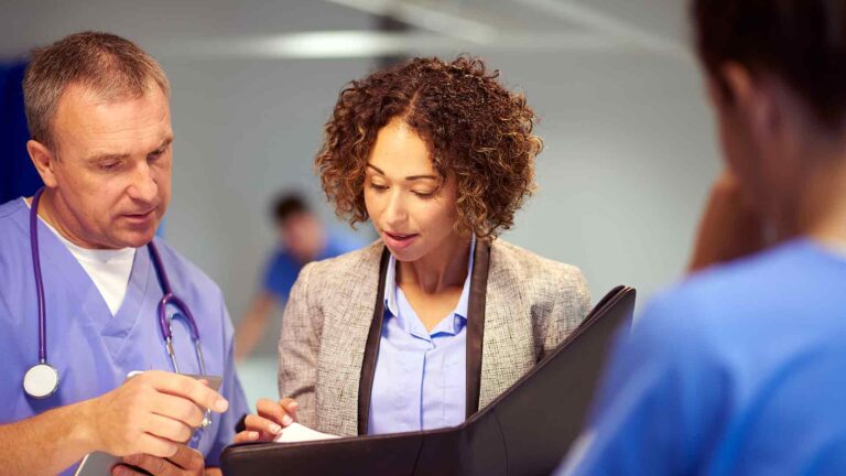 woman in blazer with clipboard conferring with two male colleagues.