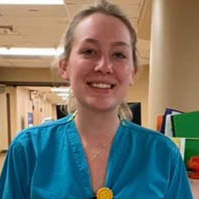 portrait of smiling woman in scrubs standing in a hospital hallway